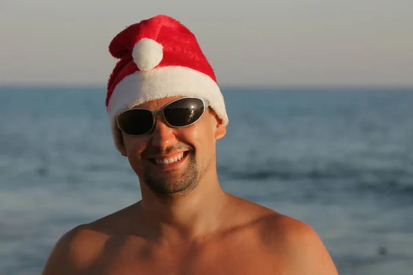 赤いクリスマス帽子とサングラス 海に対しての男性の肖像画 — ストック写真
