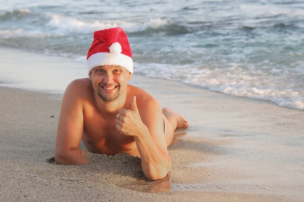 Happy new yaer on the sea: a man lying on the beach in a red Christmas hat