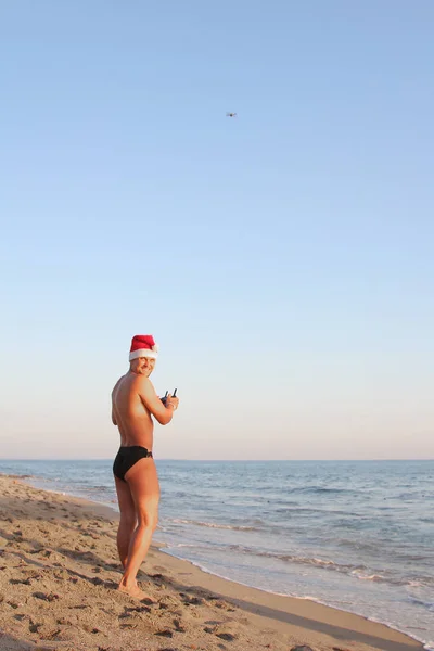 一个戴着红色圣诞帽子的人在海滩上控制着一架飞机 — 图库照片