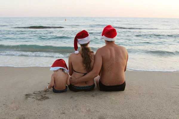 水着とビーチの砂の上に座って赤いクリスマス帽子の家族 — ストック写真