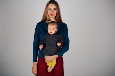 aile fotoğrafı: bir çocuk onun kollarında tutan bir kadın. Tüm aile için moda: anne ve kızı giyinmiş sarı-gri renkte. Elbise modeli gösterir