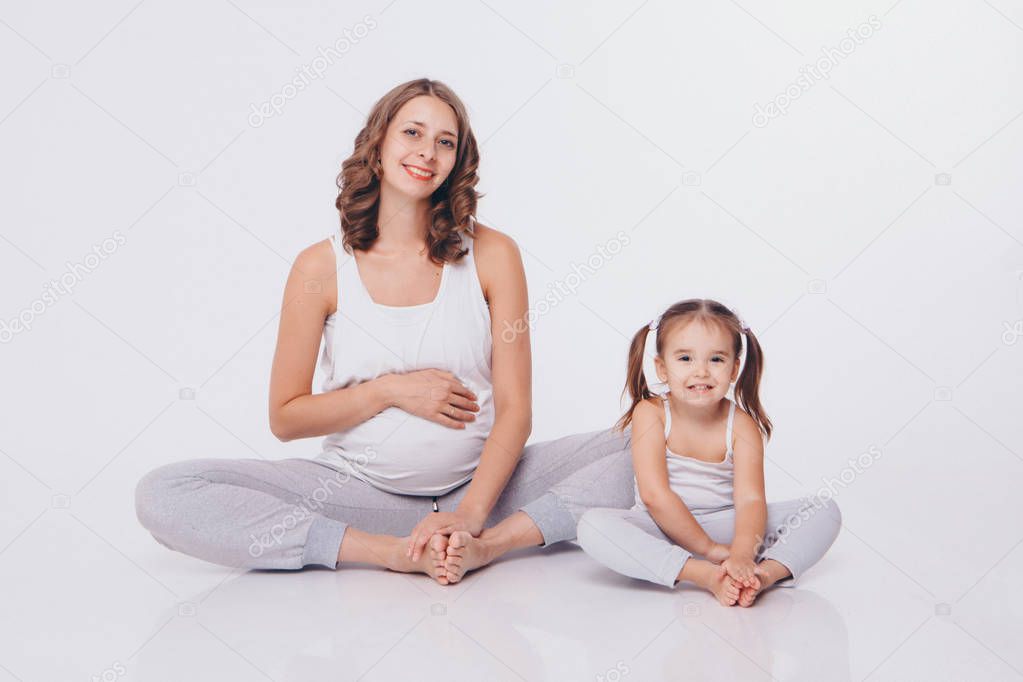international women day: pregnant woman and little girl in tracksuits sitting on the floor on white background
