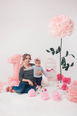 «Ana sayfa» görünümü: elbiseler içinde sayı 1, yapay çiçek ve kuş kafesi arasında katta oturan annesinin kollarında çocuk