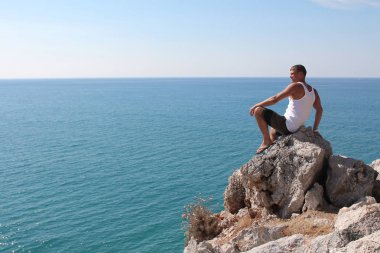 denize karşı mesafe bakarak bir kayanın üzerinde bir adam