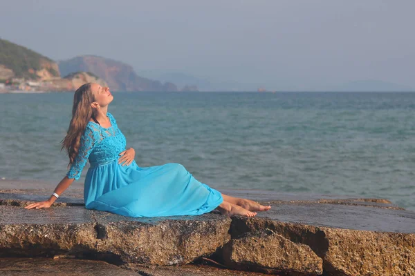 Gravid jente i blå kjole på stein ved havet – stockfoto