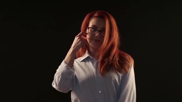 ポーズをカメラの前で黒の背景に白のシャツを着た赤い髪の美しい少女 メガネ レンズ 視力を回復するサービス モデルをアドバタイズします — ストック動画
