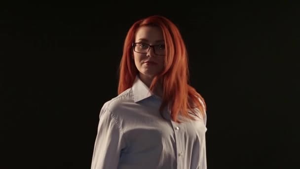 一个穿着白色衬衣的漂亮女孩 在镜头前的黑色背景上摆着一个红色的头发 该模型广告的眼镜 镜头或服务 以恢复视力 — 图库视频影像