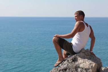 denize karşı mesafe bakarak bir kayanın üzerinde bir adam