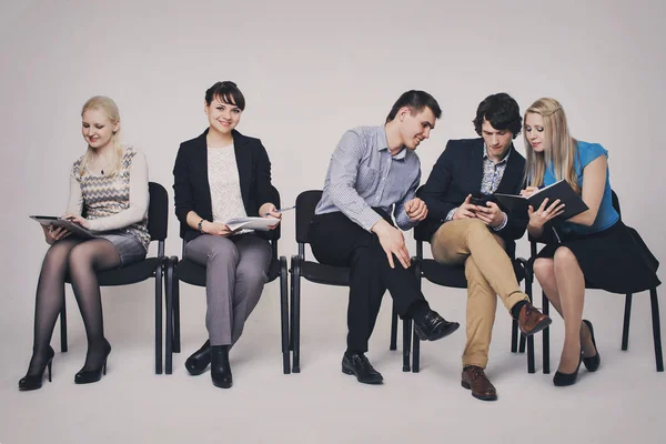 business people waiting in queue sitting in row holding smartphones and cvs, human resources, employment and hiring concept