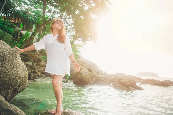 Uma mulher no glasess do sol em uma rocha que olha na distância de encontro ao mar — Fotografia de Stock