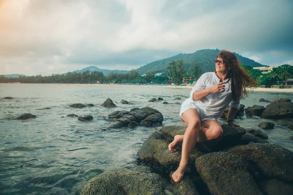 En kvinna i solen glasess på en klippa som tittar in avståndet mot havet — Stockfoto