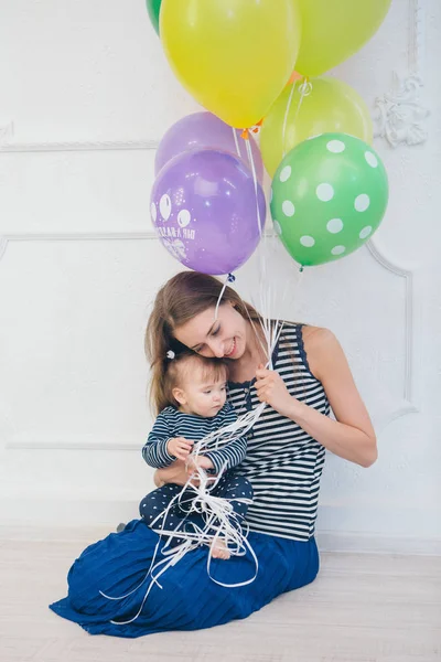 beyaz bir arka planda annesinin kollarında çocuk. Kollarında bir çocuk ile bir kadın Festival balonlar tutarak