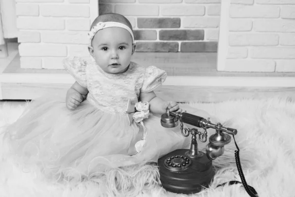 Маленькая девочка в белом платье сидит у камина рядом со старым телефоном — стоковое фото
