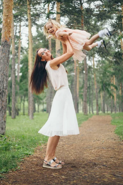 Barnet i armarna på sin mor i vit klänning. En kvinna med ett barn i famnen mot naturen — Stockfoto