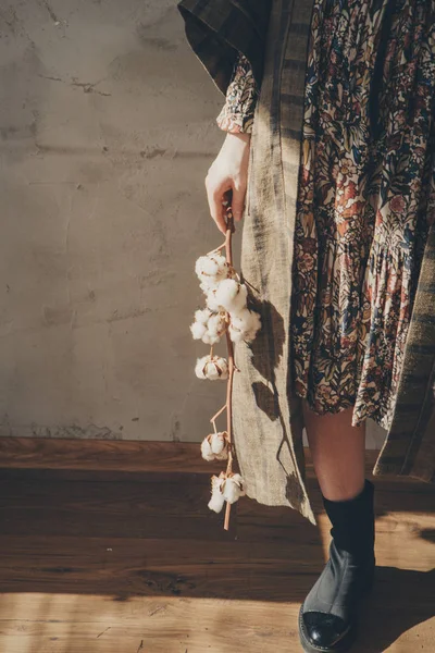 women\'s feet in linen clothes and shoes next to a flower on a white background