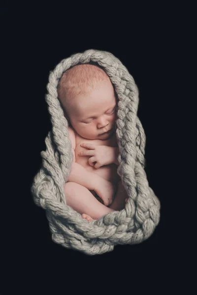 Bebê recém-nascido nu dorme enrolado em uma bola em uma corda trançada no fundo preto — Fotografia de Stock