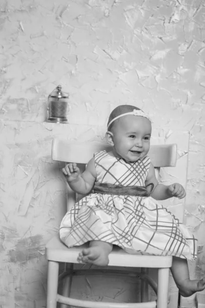 Uma menina em um vestido senta-se em uma cadeira e sorri — Fotografia de Stock