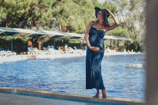 Mulher grávida com cabelos longos em vestido azul posando na água — Fotografia de Stock