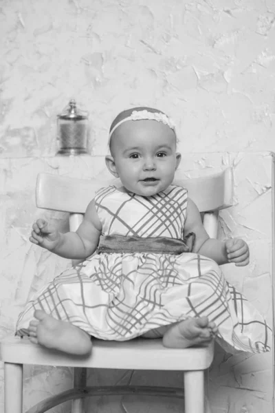 A little girl in a dress sits on a chair and smiles — Stock Photo, Image