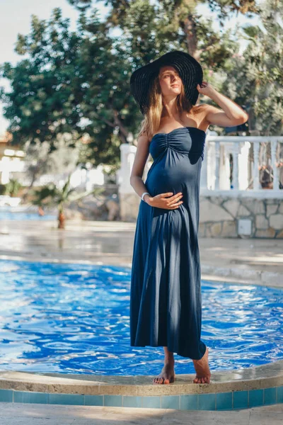 Mulher grávida com cabelos longos em vestido azul posando na água — Fotografia de Stock