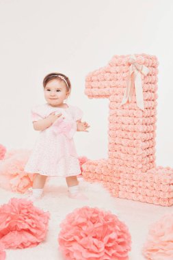 Doğum günü kutlaması: kız numaraları 1, yapay çiçekler ve kuş kafesi arasında yerde oturan