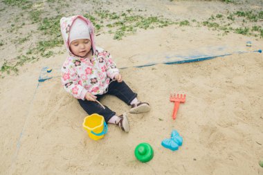 Küçük kız kum havuzunda oturan ve kum da oynayan Oyun alanı küçük çocuk üzerinde kalıp ile oynuyor