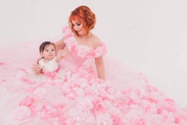 çiçek pembe bir elbise annesinin kollarında çocuk. Beyaz bir arka planda kollarında çocuk olan bir kadın, izole