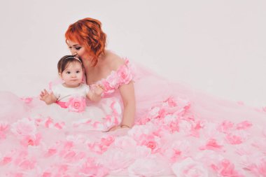 çiçek pembe bir elbise annesinin kollarında çocuk. Beyaz bir arka planda kollarında çocuk olan bir kadın, izole