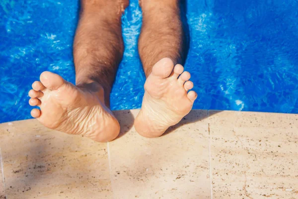 Blijf in het resort. Mannen benen op een grote waterachtergrond. Een zwemmende man in het zwembad. Het concept van recreatie, ontspanning, toerisme. — Stockfoto