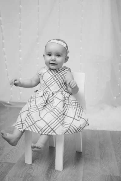 Маленькая девочка в платье сидит на стуле и улыбается — стоковое фото