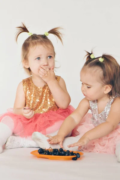 Due bambine che mangiano uva sedute sul pavimento su uno sfondo bianco — Foto Stock