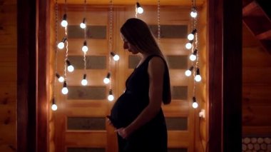 gölgede uzun saçlı hamile bir kadın lambalar bir çelenk arka planda midesini okşayarak. Tıp ve dekoratif unsurlar