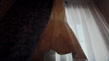 pencerenin yanında bir askı asılı beyaz gelinlik