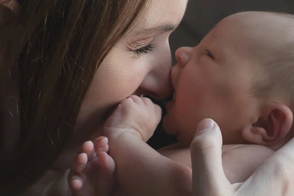 Dziecko w ramionach matki. Kobieta trzyma dziecko twarzą w twarz. Dziewczyna gryzie jej nos — Zdjęcie stockowe