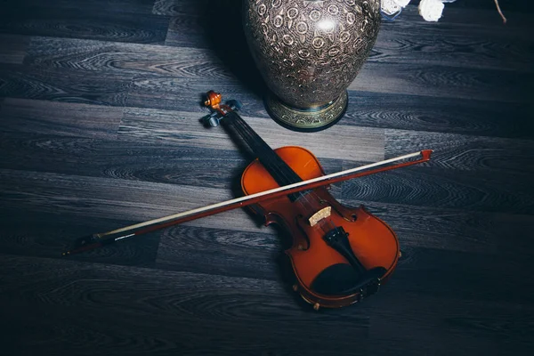 Crepúsculo: arco e violino deitado no chão ao lado de um vaso decorativo e flores — Fotografia de Stock