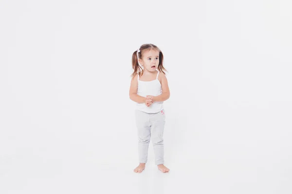 Маленька дівчинка захоплюється білим тлом: танцює, сором'язлива, показує великий палець — стокове фото