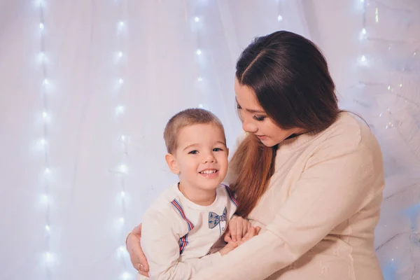 Das Kind in den Armen seiner Mutter auf dem Hintergrund von Lichtern und dekorativen Elementen — Stockfoto