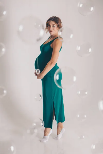 Felice donna incinta in abito verde impegnata in ginnastica ricreativa. Isolato su sfondo bianco — Foto Stock