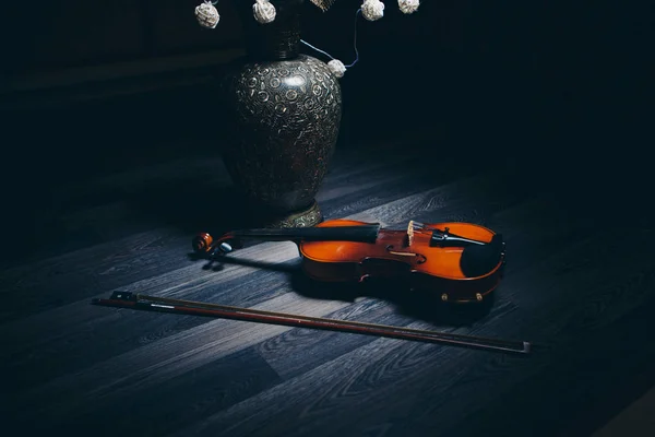 Свет: бант и скрипка лежат на полу рядом с декоративной вазой и цветами — стоковое фото