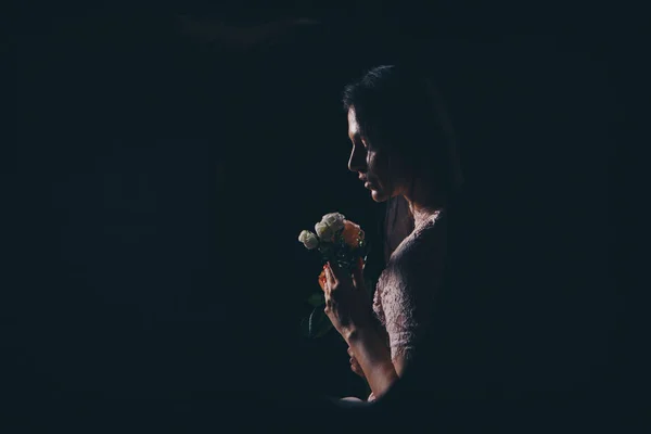 Profilo di una donna con fiori su sfondo nero. La ragazza annusa le rose. Silhouette di una signora al buio — Foto Stock
