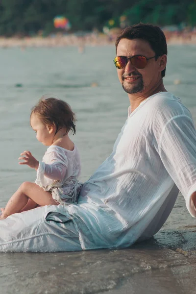 Güneş gözlüğü baba plaj arka planda bebeği kollarında tutar. Genç çocukların babasını eğitmek kavramı, mutlu çocukluk, dostça bir aile. — Stok fotoğraf