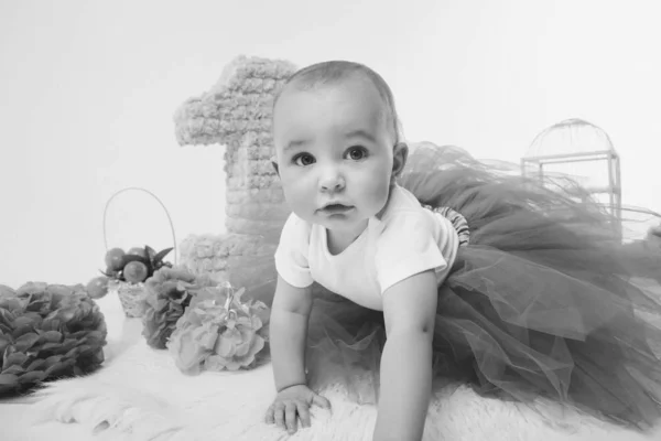 Birthday celebration: girl sitting on the floor among the numbers 1, artificial flowers and bird cage — Stock Photo, Image