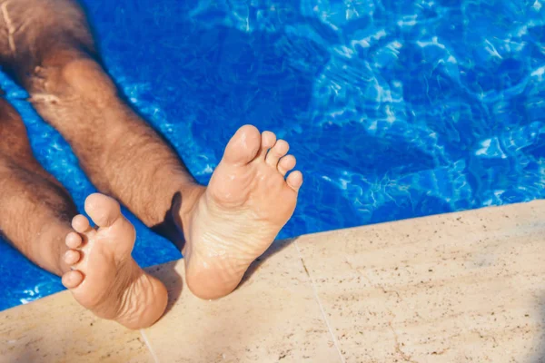 Bleiben Sie im Resort. Männerbeine vor großem Wasserhintergrund. Mann schwimmt im Pool. Das Konzept der Erholung, Entspannung, des Tourismus. — Stockfoto