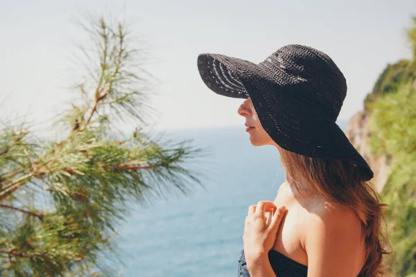 Retrato de um turista com cabelos longos em chapéu preto contra as rochas e o mar. mulher em viagem — Fotografia de Stock