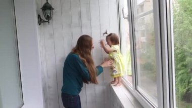 Küçük bir kız pencere den annesinin ellerine atlamak öğrenir. Kadın çocuğu yakalıyor.