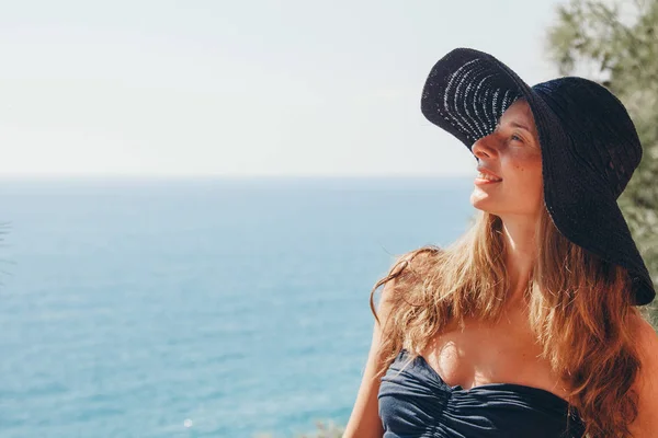 Retrato de um turista com cabelos longos em chapéu preto contra as rochas e o mar. mulher em viagem — Fotografia de Stock