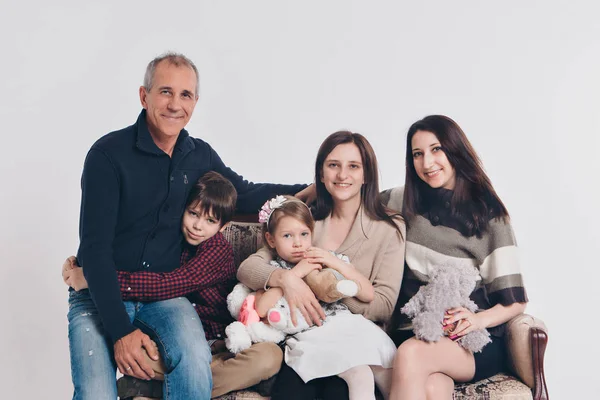 Concepto de infancia feliz, familia, amor - grupo de personas sobre un fondo blanco: adultos y niños con juguetes sentados en el mismo sofá — Foto de Stock