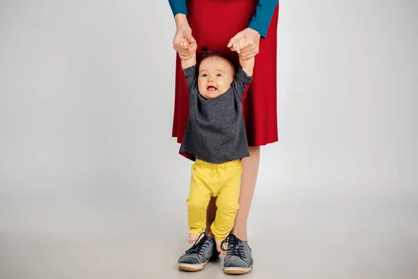 Bebê bonito aprender a andar e fazer seus primeiros passos. A mãe está a segurar-lhe a mão. pés de criança perto, espaço de cópia — Fotografia de Stock