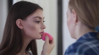 bir kız başka bir kıza makyaj uygular. model ateş etmeye hazırlanıyor. makyaj sanatçısı tarafından makyaj uygulaması