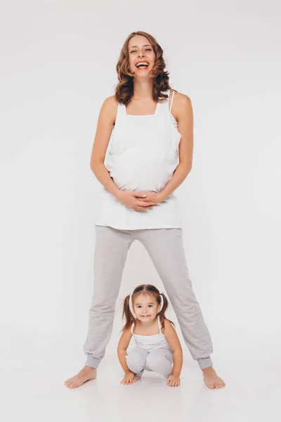 Η μαμά και η κόρη διασκεδάζουν σε λευκό φόντο. Η έγκυος γυναίκα και το παιδί παίζουν μαζί. έννοια της παιδικής ηλικίας, της υγειονομικής περίθαλψης, της γονιμοποίησης — Φωτογραφία Αρχείου